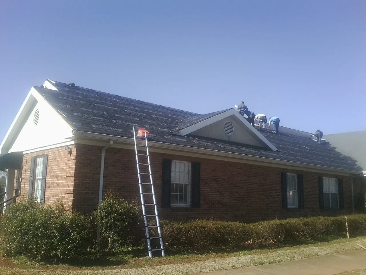 Crew tearing shingles off a brick ranch roof with a ladder set — Emergency Roof Repair work by our crew in Post Falls