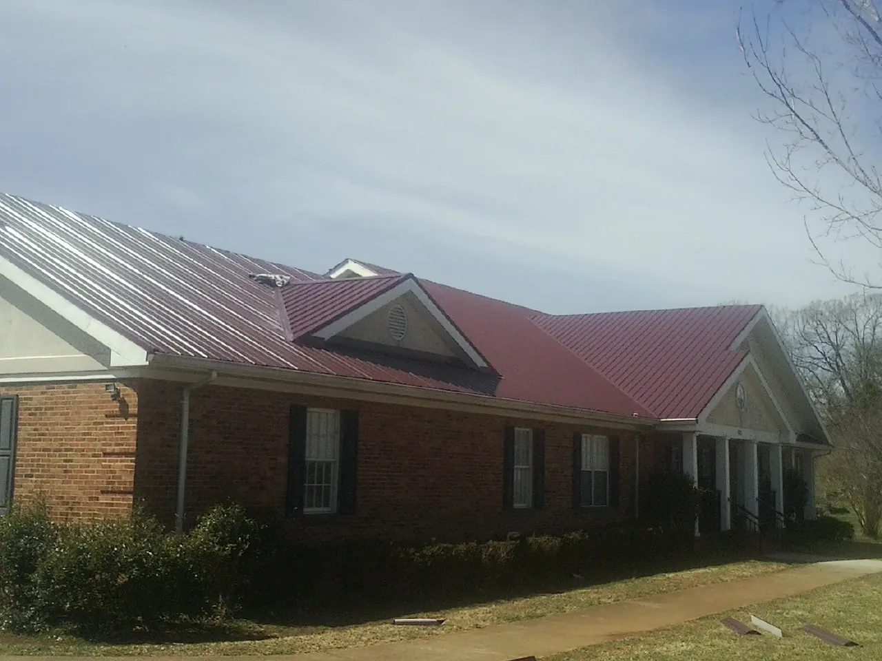 Red metal roof with gabled entries on a long brick building, from a Hail Damage Roof Repair job in Post Falls