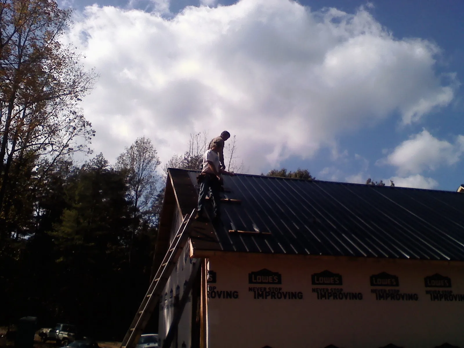 Roofer fastening dark metal panels high against a cloudy sky, from a Roof Inspection job in Post Falls